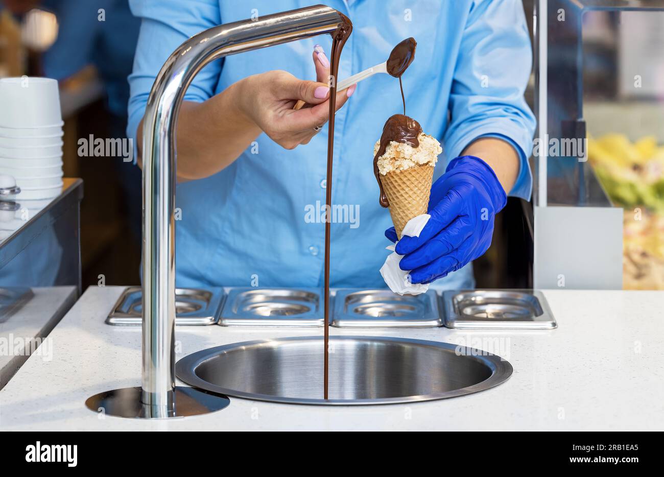 Venditore in una pasticceria che prepara il cioccolato su un gelato alla vaniglia con un cucchiaino Foto Stock