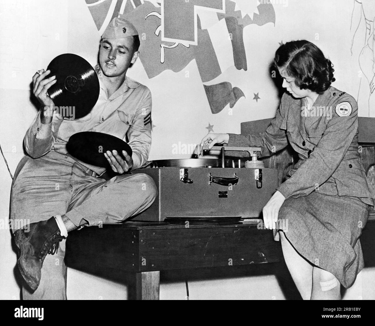 South Pacific: c. 1944 A U.S, Marine Corps sargeant e un membro dello staff della Croce Rossa scelgono record di 78 giri per giocare nella sala giochi di un American Red Cross Service Club. Foto Stock