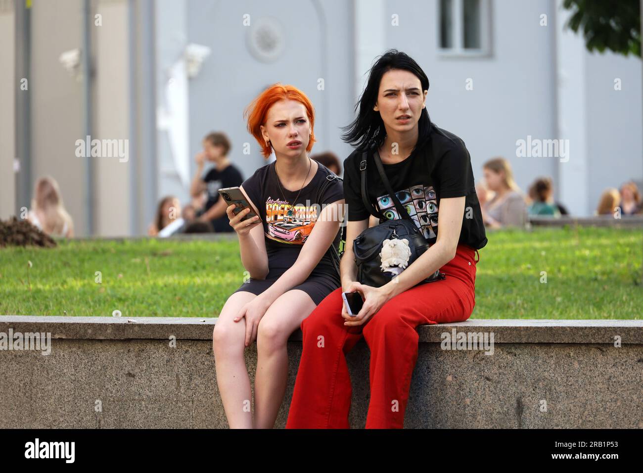Due ragazze sedute per strada con gli smartphone. Ragazza con i capelli tinti nella città estiva Foto Stock