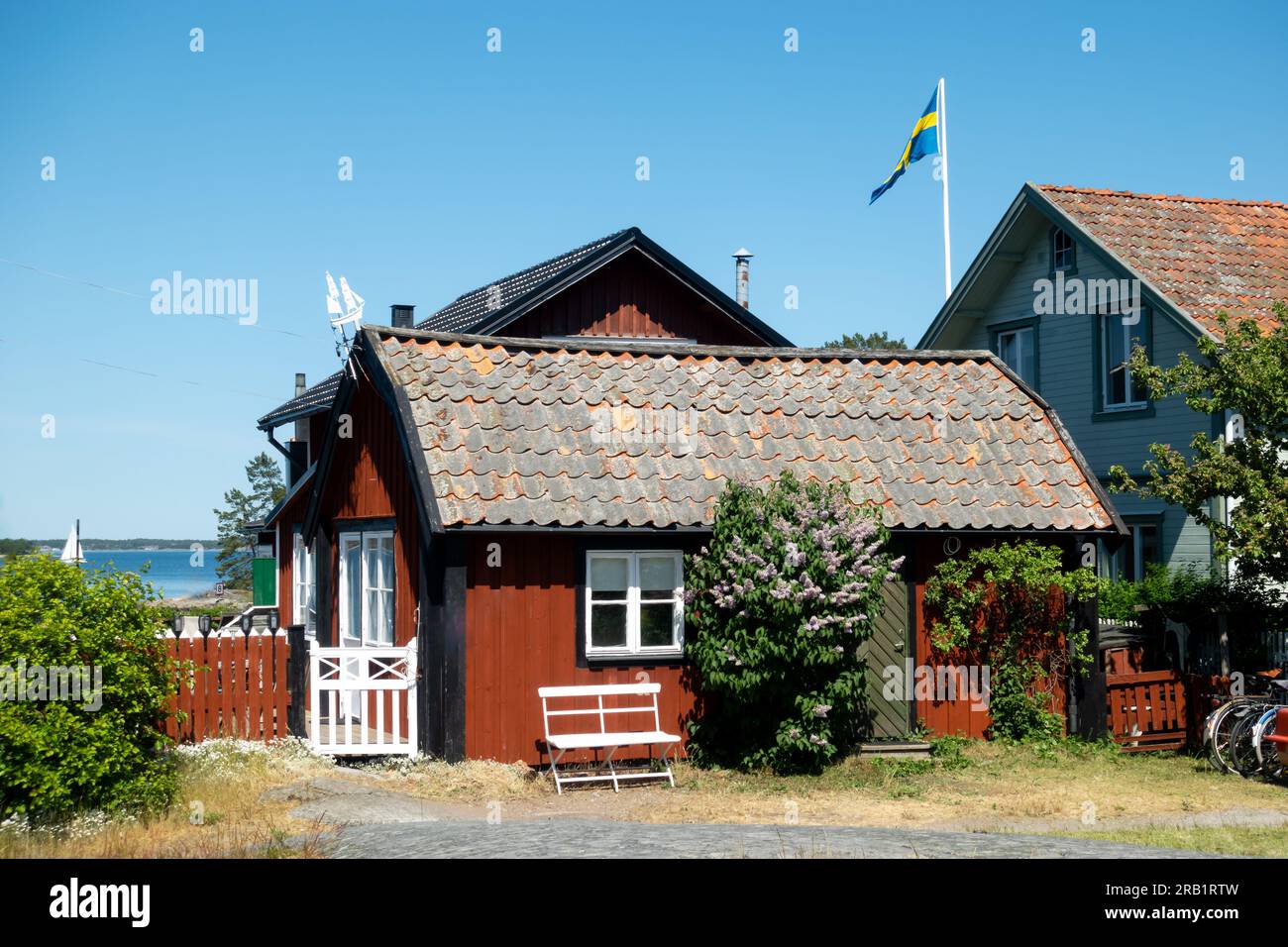 Tipica casa rossa di falu in Svezia con angoli bianchi su una pittoresca isola rurale di un villaggio di pescatori nell'arcipelago di Stoccolma con bandiera svedese Foto Stock