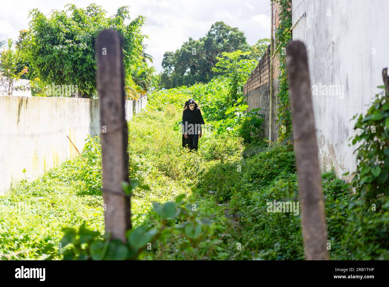 Santo Amaro, Bahia, Brasile - 24 luglio 2022: Una persona cammina tra le piante vestite di nero con una maschera di terrore durante una manifestazione culturale in Foto Stock