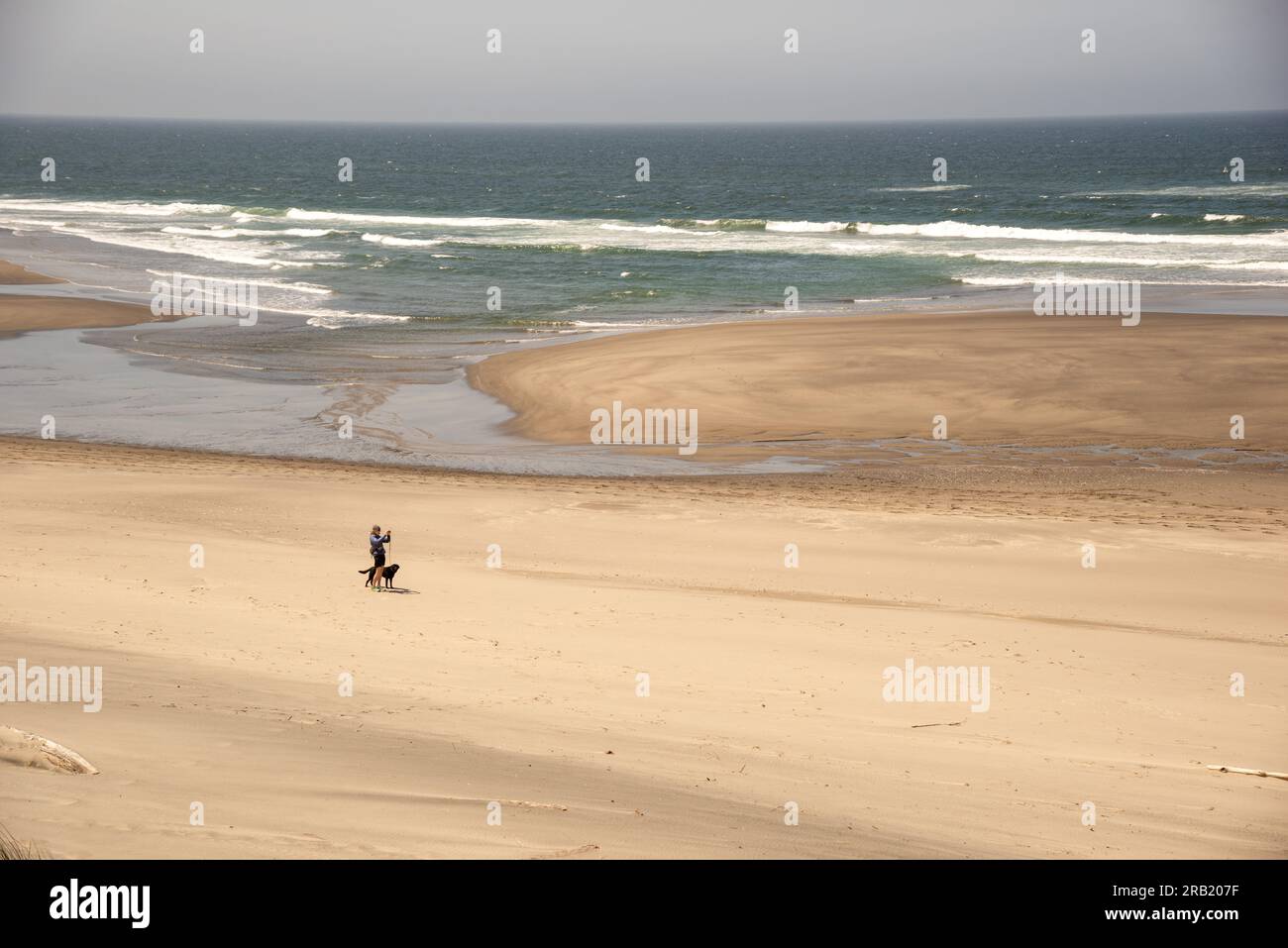 Donna che cammina con un cane che fa un selfie lungo la costa dell'Oregon. Foto Stock