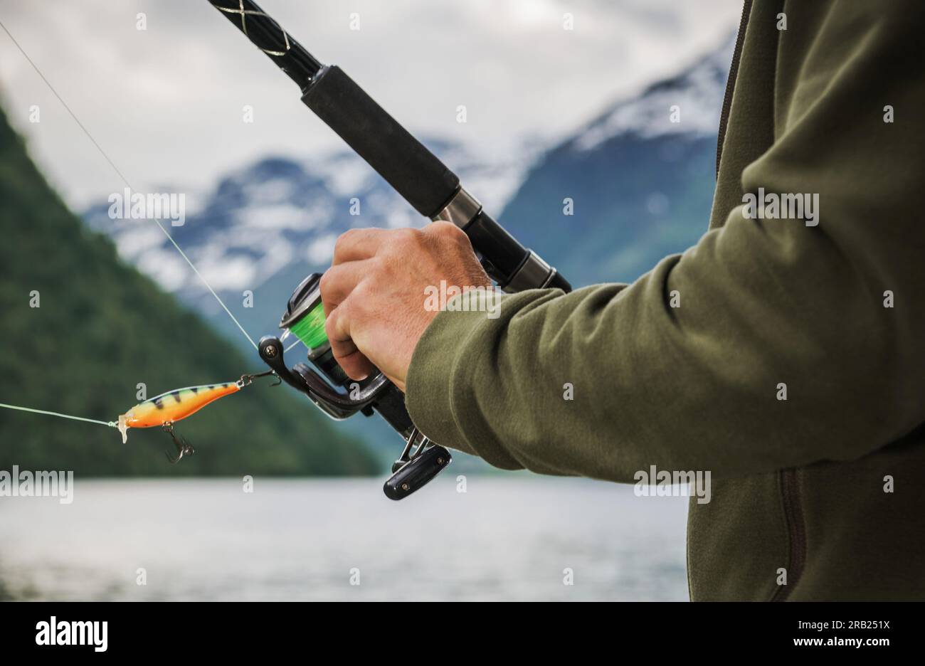 Primo piano di Fisherman Hand per prepararsi a preparare una canna da pesca con bobina di filatura. Paesaggio montano sullo sfondo. Foto Stock