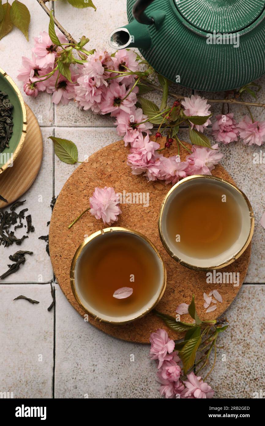 Cerimonia tradizionale. Tazza di tè estratto, teiera, foglie essiccate e  fiori sakura su un tavolo piastrellato, piatto Foto stock - Alamy