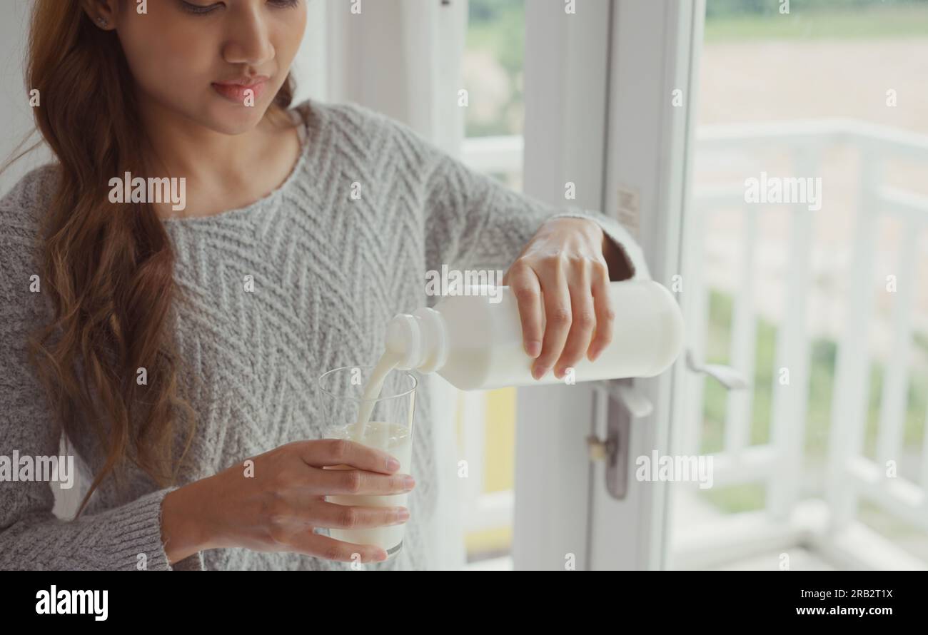 Giovane donna che versa latte nel bicchiere. Foto Stock