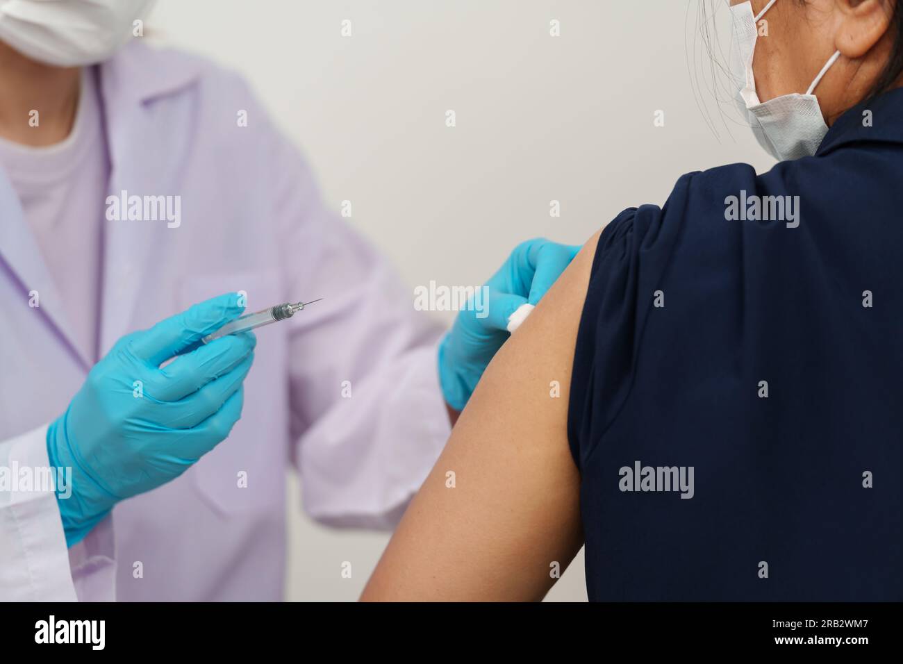 medico che tiene la siringa e che usa il cotone prima di fare l'iniezione al paziente in una maschera medica. Vaccino Covid-19 o coronavirus Foto Stock