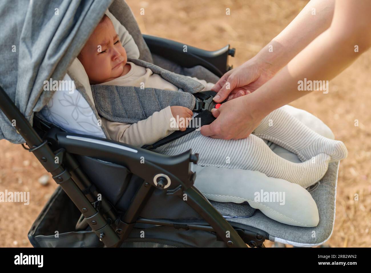 donna che fissa la cintura al passeggino con il bambino che piange Foto Stock