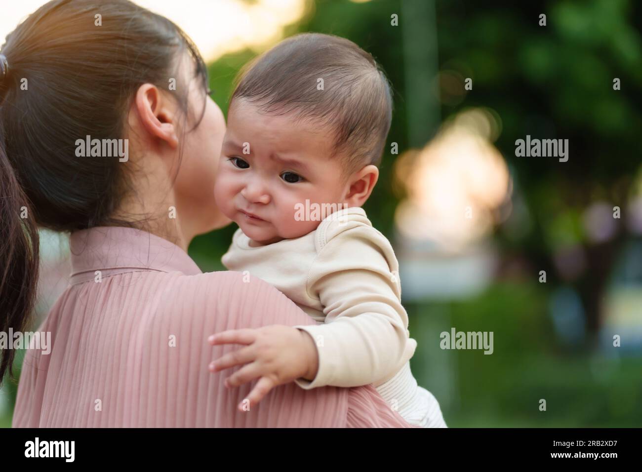 la madre tiene in mano e conforta il bambino piangente all'aperto nel parco con la luce del sole Foto Stock