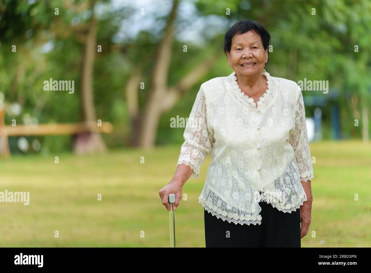 donna anziana felice con bastone da passeggio nel campo d'erba del parco Foto Stock