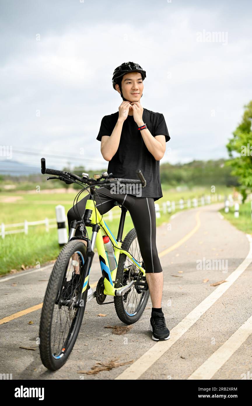 Un ritratto di un giovane asiatico felice e affascinante che indossa abbigliamento sportivo togliendosi il casco da bici dopo aver messo in bicicletta il casco prima di andare in bicicletta Foto Stock