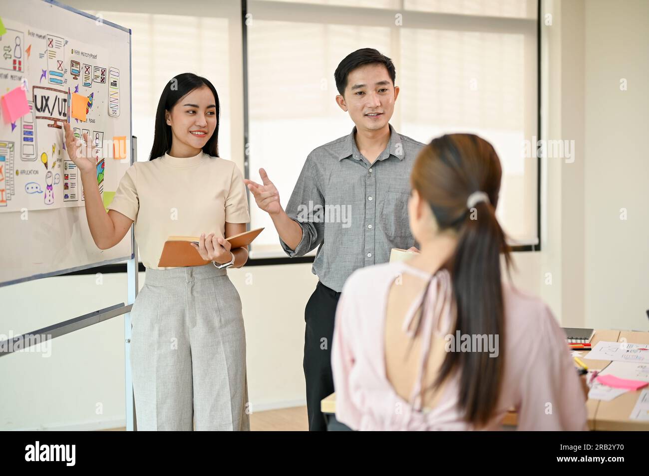 Due sviluppatori di tecnologia asiatici professionisti stanno presentando il loro nuovo progetto al loro team durante l'incontro. Azienda di startup tecnologica, UI, UX Foto Stock