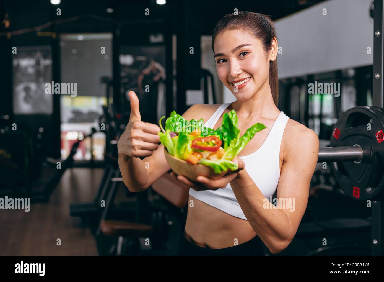 giovane donna sportiva asiatica in fitness club sportivo con cibo sano mangiare verdure mescolare insalata dieta a basso contenuto calorico Foto Stock
