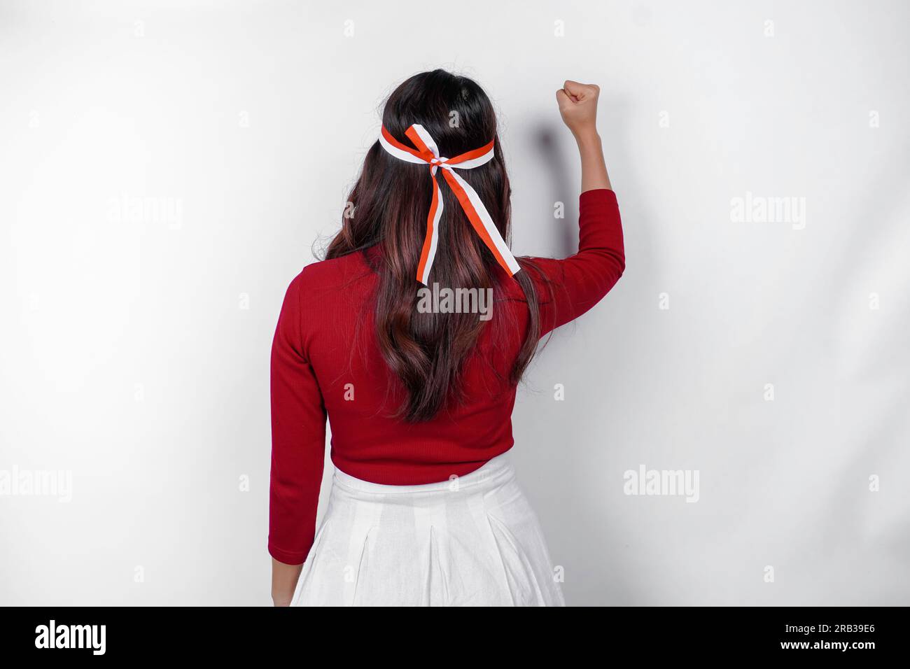 Vista posteriore di una giovane donna asiatica con un gesto felice di successo che indossa la parte superiore rossa e la fascia con bandiera isolata da uno sfondo bianco. L'independe dell'Indonesia Foto Stock