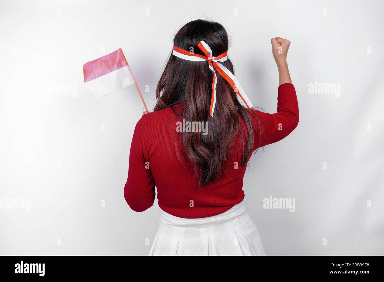 Vista posteriore di una giovane donna asiatica con un gesto felice di successo che indossa la parte superiore rossa e la fascia con bandiera isolata da uno sfondo bianco. L'independe dell'Indonesia Foto Stock