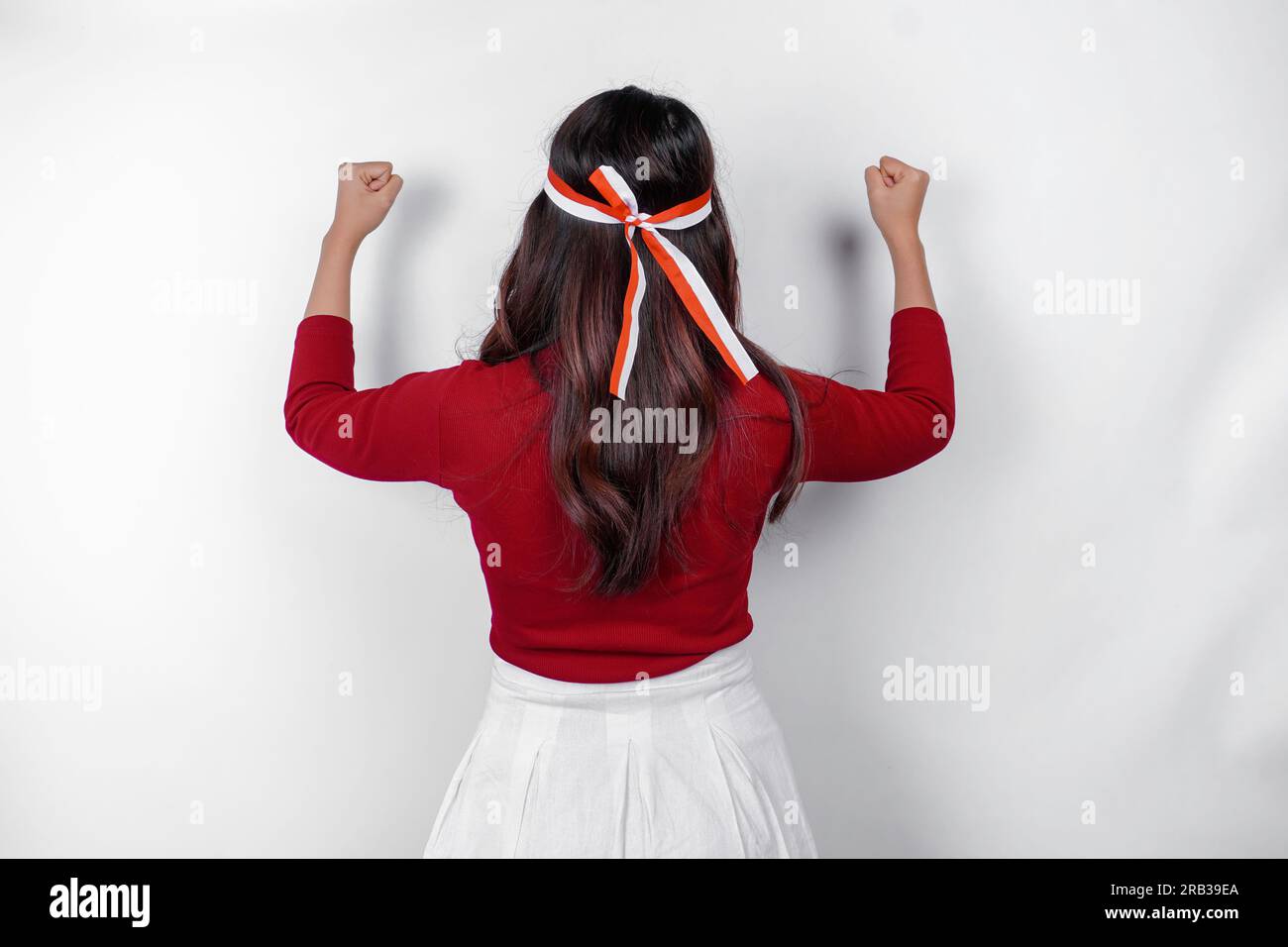 Vista posteriore di una giovane donna asiatica con un gesto felice di successo che indossa la parte superiore rossa e la fascia con bandiera isolata da uno sfondo bianco. L'independe dell'Indonesia Foto Stock