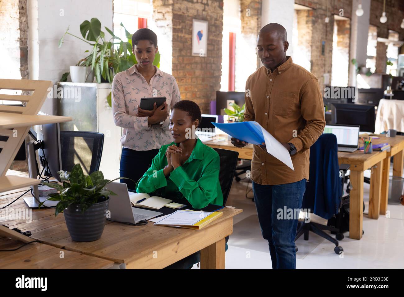 Colleghi afroamericani impegnati che utilizzano il computer con documenti in ufficio creativo. Business, tecnologia e lavoro di squadra, inalterati. Foto Stock