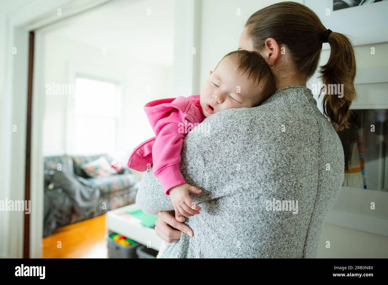 La bambina dorme sulla spalla della mamma mentre viene tenuta a casa Foto Stock