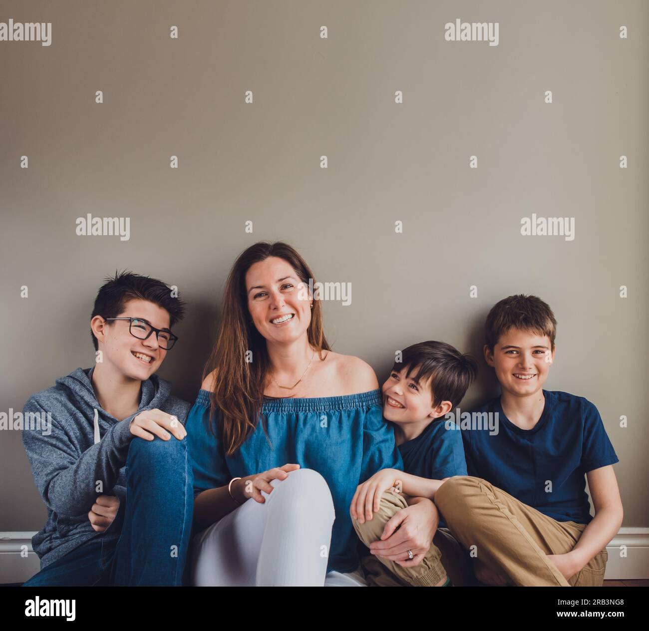 Madre e i suoi tre ragazzi seduti a terra contro un muro liscio. Foto Stock