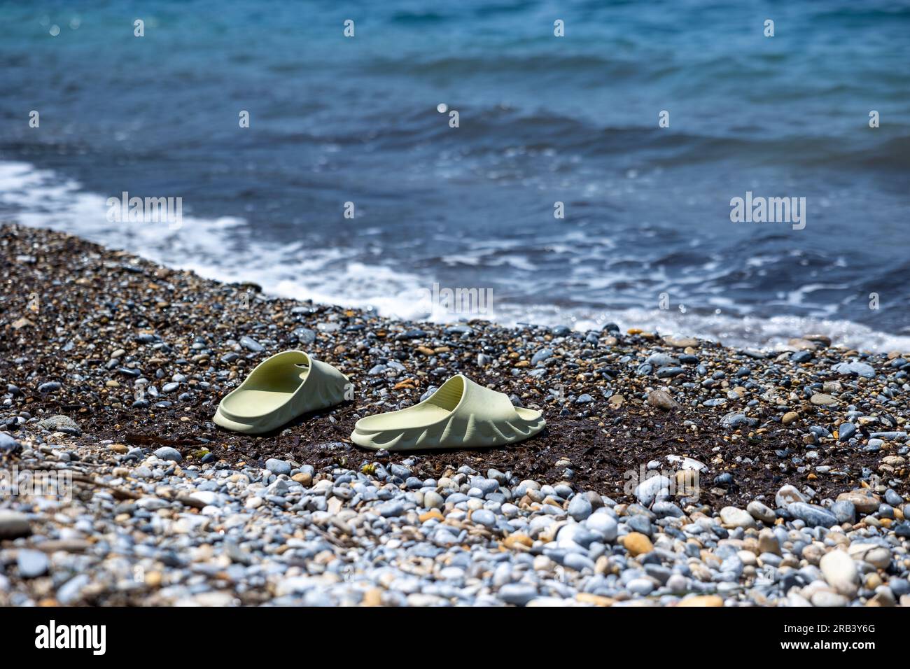 Sabbia, mare blu e pantofole bianche e verdi. Concentrati sulle pantofole. Turkiye Resort Foto Stock