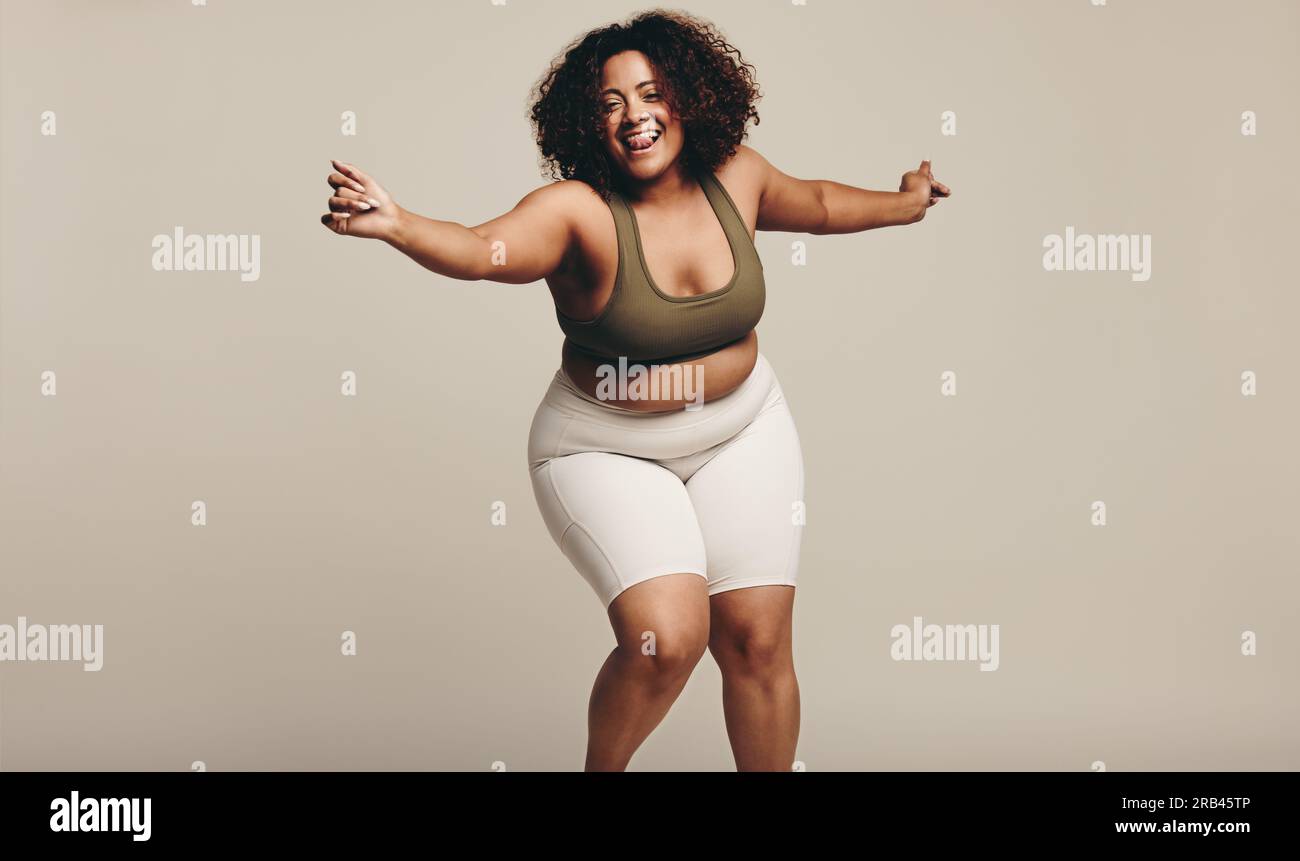 Donna che balla in studio, muovendo il suo corpo con un sorriso felice mentre trova il suo ritmo. Donna che esprime fiducia nei suoi movimenti del corpo senza sforzo, e. Foto Stock