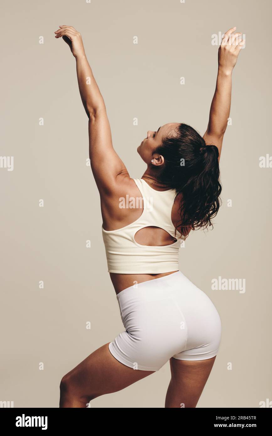 Vista posteriore di una giovane donna attiva e in forma che mostra i suoi muscoli tonici e la sua forma atletica attraverso il movimento del corpo. Donna che indossa abbigliamento sportivo Foto Stock