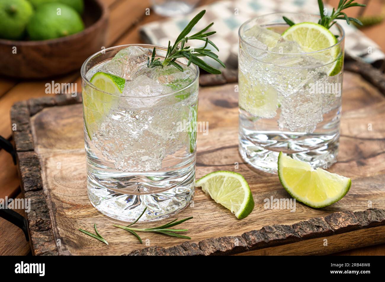 Gin e cocktail tonico guarnito con spicchi di lime e rosmarino su un vassoio rustico di legno Foto Stock