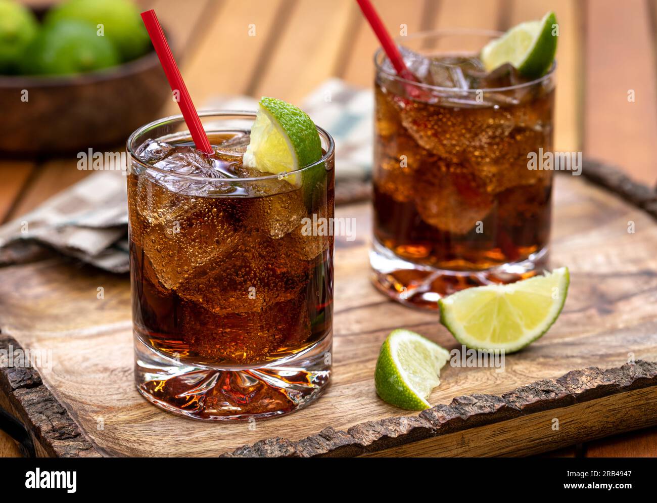 Cocktail al rum e cola con fette di ghiaccio e lime su un vassoio di legno rustico Foto Stock