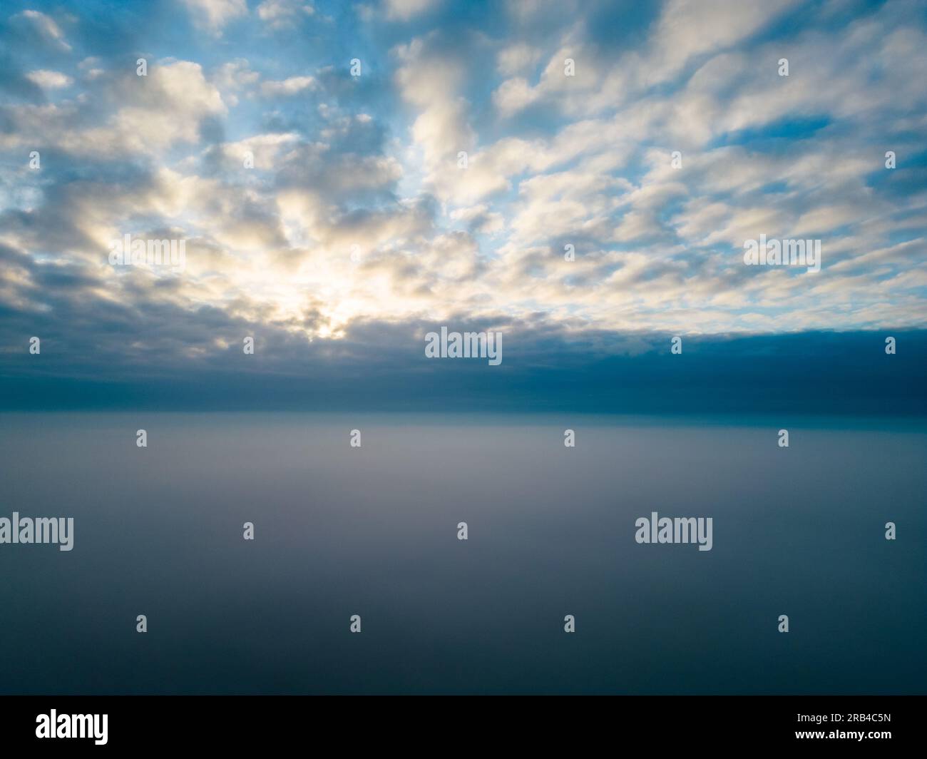 Una suggestiva foto aerea cattura lo spettacolo mozzafiato del sole che sorge sopra una lussuosa coperta di nuvole. L'immagine eterea evoca un travolgente senso di pace, vastità e la grandezza dei miracoli quotidiani della natura. Vista aerea: Maestosa alba sopra le nuvole. Foto di alta qualità Foto Stock