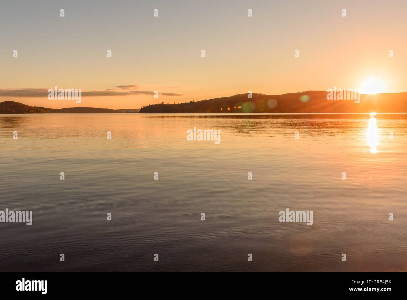 Tramonto su un lago con coste boscose in cima al fogliame autunnale Foto Stock