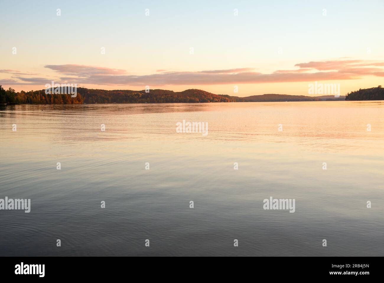 Vista di un lago con rive boscose al tramonto, al culmine dei colori autunnali. Scena tranquilla. Foto Stock