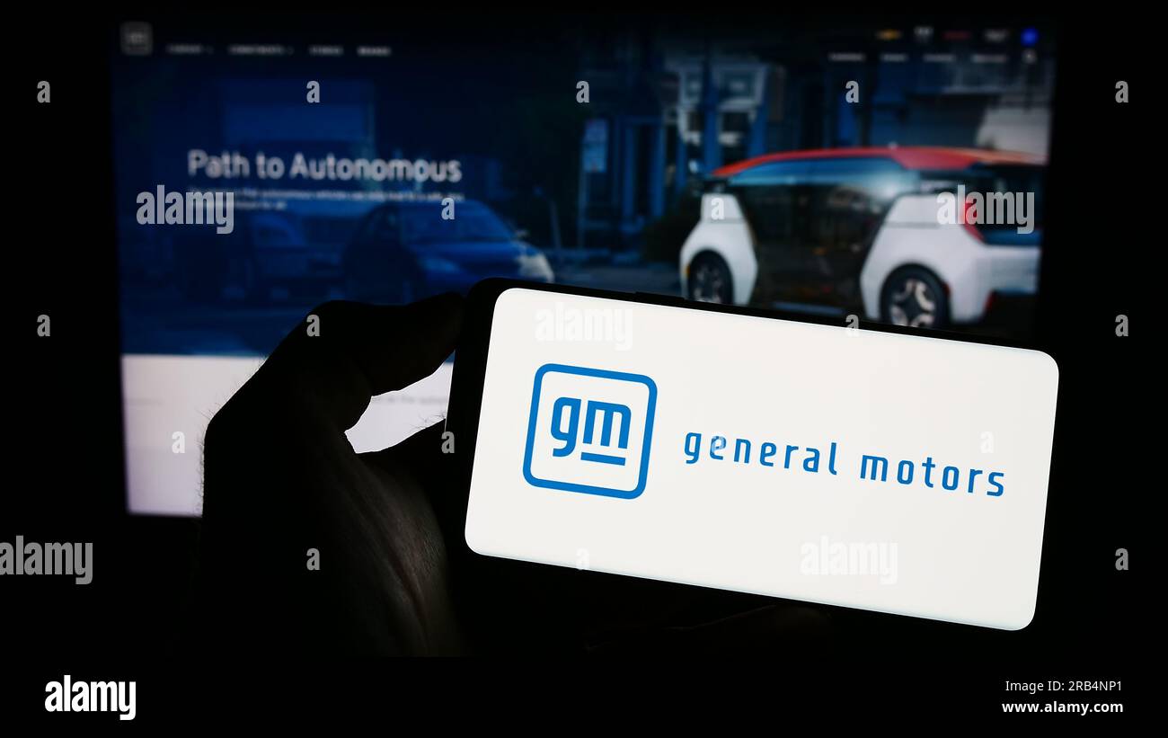 Persona in possesso di un cellulare con il logo del produttore automobilistico statunitense General Motors Company (GM) sullo schermo davanti alla pagina Web. Concentrarsi sul display del telefono. Foto Stock