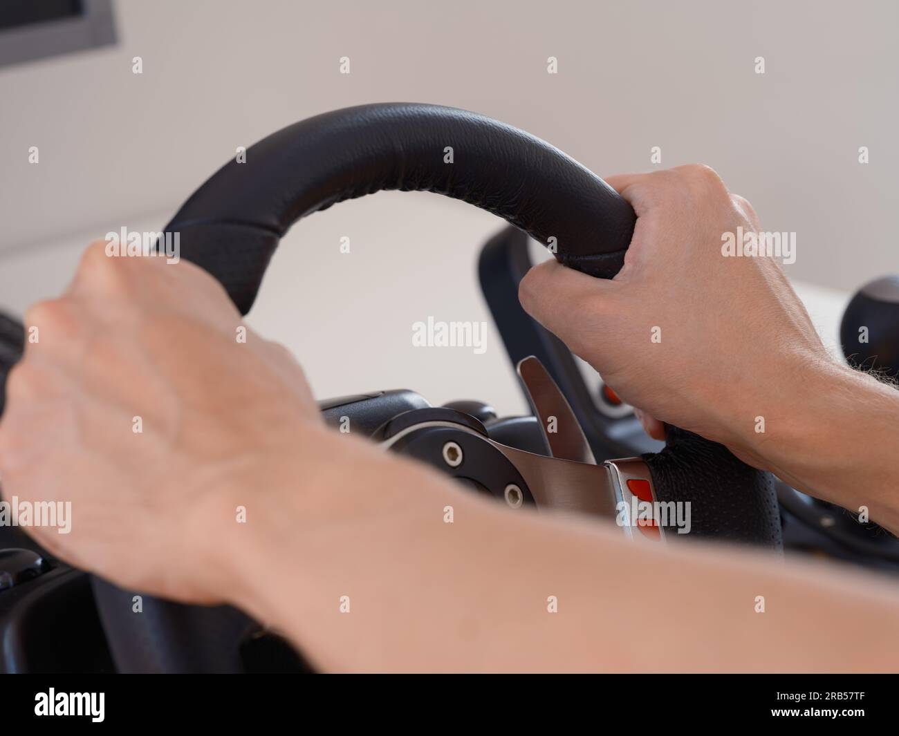 Una persona seduta dietro un computer che tiene in mano il volante di un simulatore di guida. Primo piano. Foto Stock