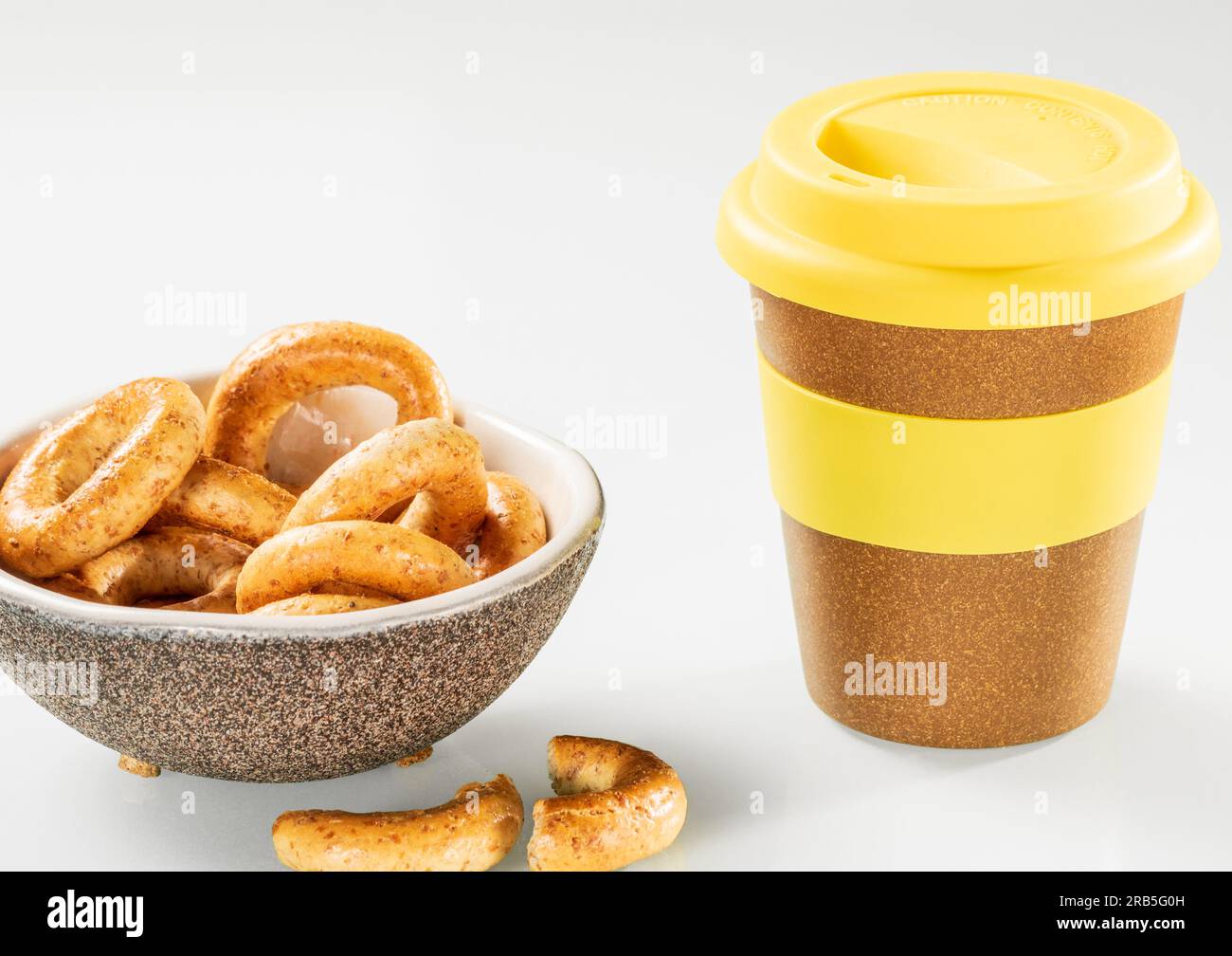 Tazza di caffè in plastica e piattino con bagel su sfondo bianco. Foto Stock