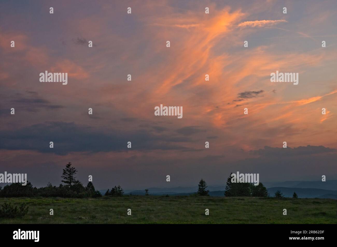 Nuvola di Cirro, arancione dall'ultima luce del sole che tramonta, sopra un paesaggio collinare nei Vosgi Foto Stock