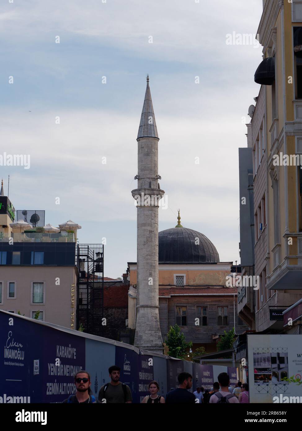 Piccola e semplice moschea nel quartiere Karakoy di Istanbul accanto a un edificio con terrazza sul tetto mentre la gente cammina nella strada sottostante. Istanbul Foto Stock