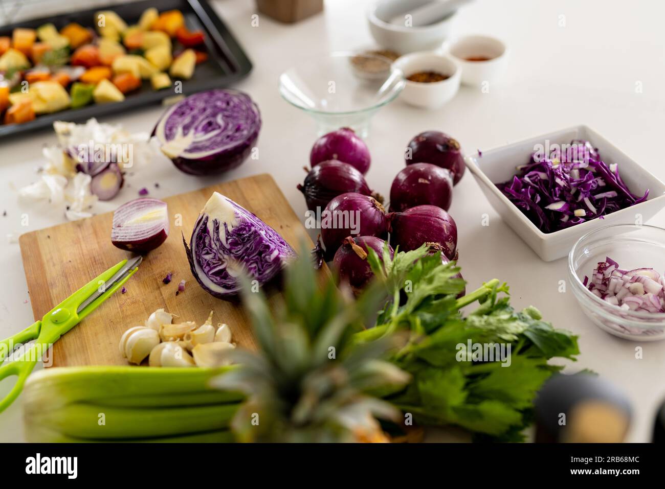 Verdure su tagliere e verdure tritate in vassoio da forno sul piano di lavoro nella cucina soleggiata. Cucina, cibo, ingredienti, vita sana e domesti Foto Stock