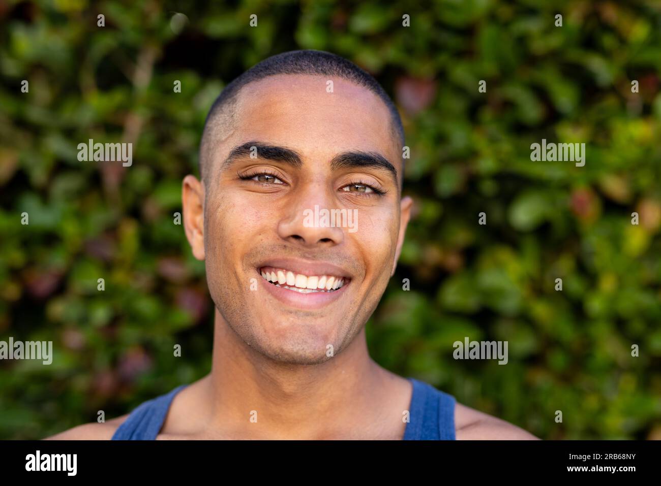 Ritratto di un uomo birazziale felice con i capelli tagliati a bocca aperta sorridendo nel soleggiato giardino. Estate, tempo libero, benessere e stile di vita, inalterati. Foto Stock