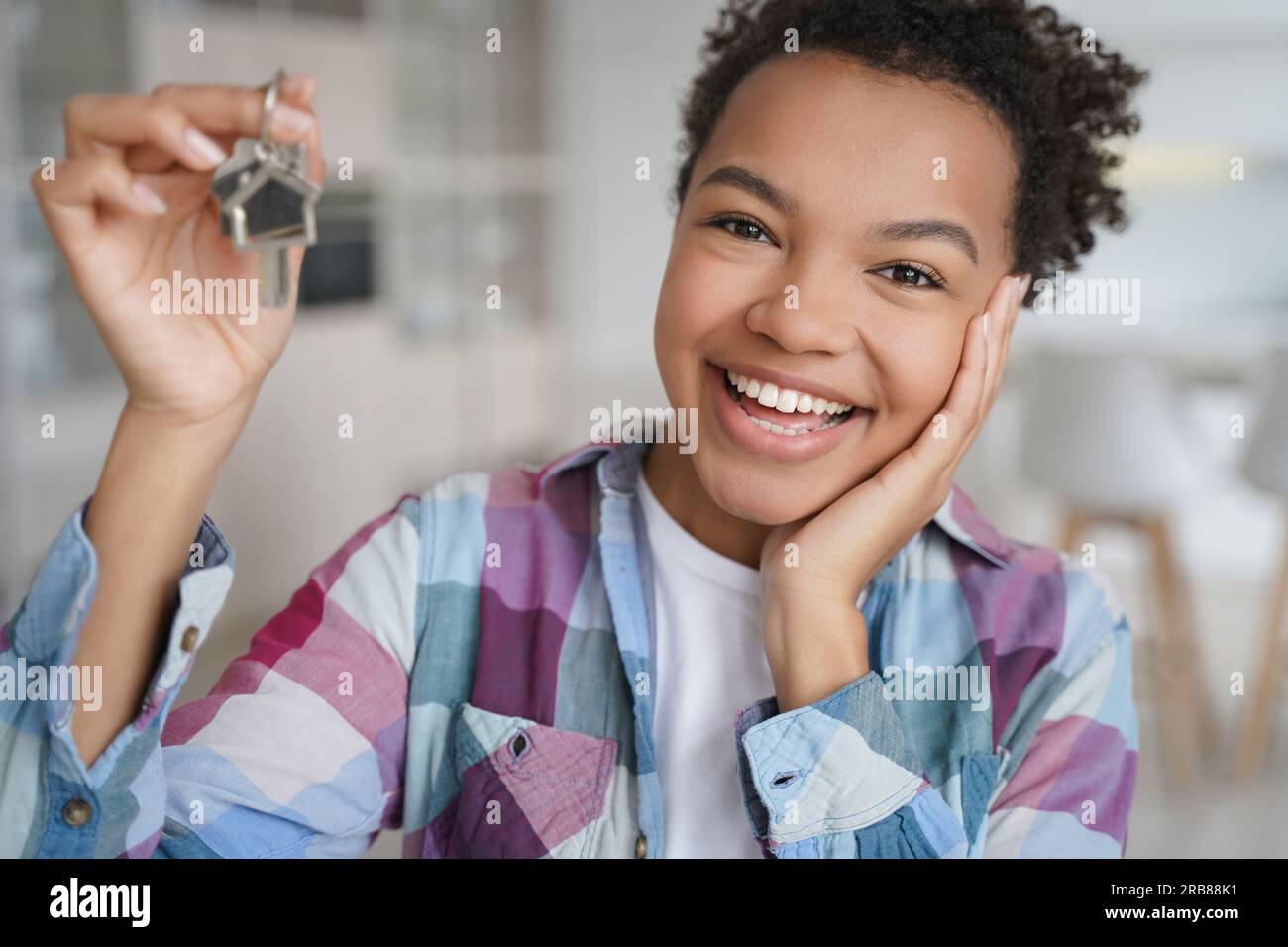 Un adolescente birazziale entusiasta mostra con orgoglio le chiavi della nuova casa, abbracciando l'indipendenza dai genitori. Foto Stock