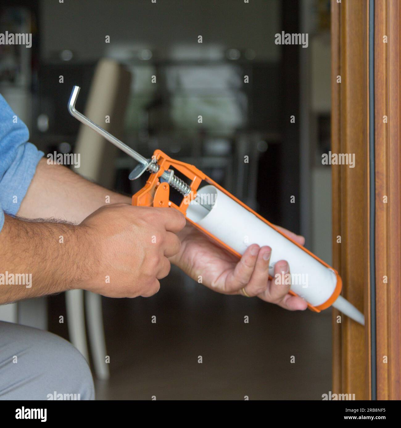 Immagine delle mani di un tuttofare che con una pistola al silicone installa e sigilla porte e finestre contro le correnti d'aria. Miglioramenti all'isolamento termico domestico. Foto Stock