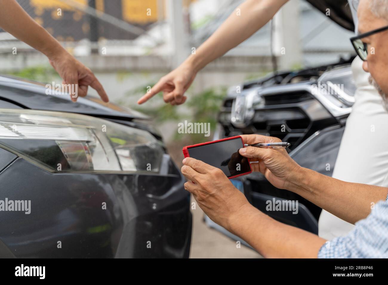 Un agente di assicurazione auto maschile che usa il suo telefono per scattare foto dei segni dell'incidente, mentre i proprietari di auto maschi e femmine indicano la Foto Stock
