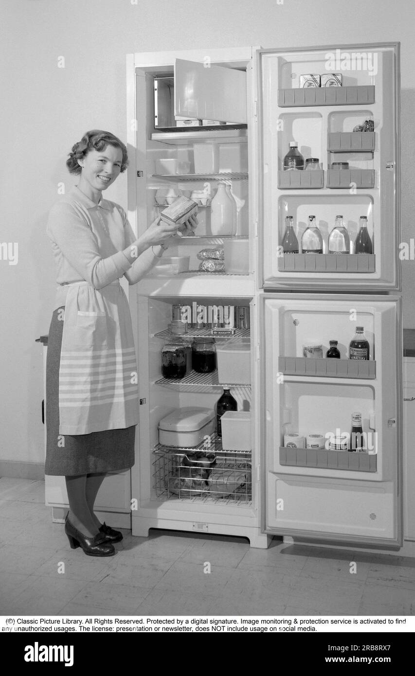In cucina anni '1960 Una donna nella sua cucina con la porta aperta sul frigorifero. Puoi vedere i prodotti alimentari di vari tipi che sono ordinatamente esposti sugli scaffali. Tra le altre cose, è visibile il classico pacchetto di latte Tetran. Inventato da Ruben Rausing e che divenne l'inizio dell'impero del packaging Tetra Pak. Svezia 1960. Rif. Conard 4188 Foto Stock