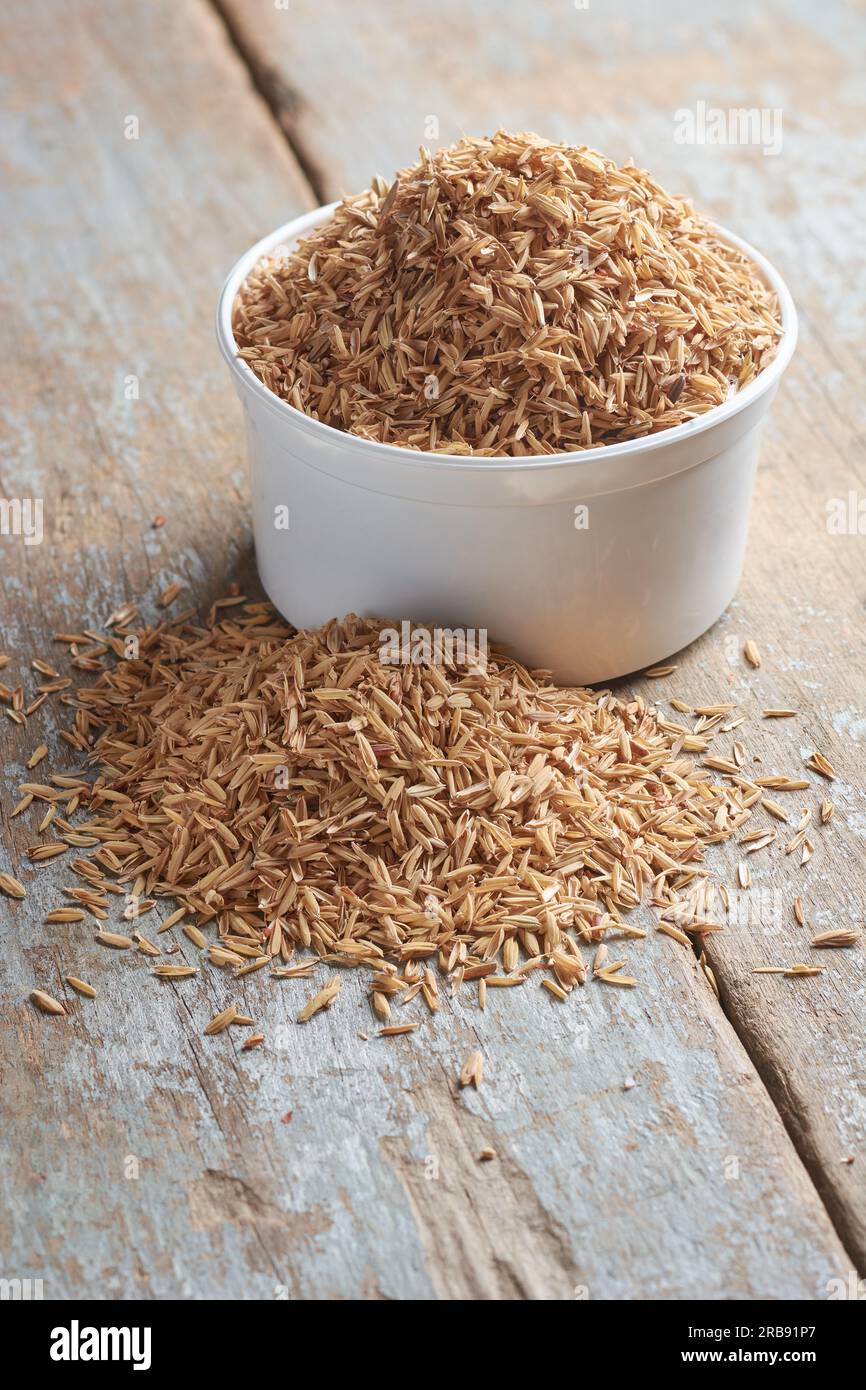 coppa di buccia di risone o di riso, detta pula di riso gialla, buccia di riso o scafo di riso, strato più esterno del chicco di riso da utilizzare come alimentazione animale, su legno Foto Stock