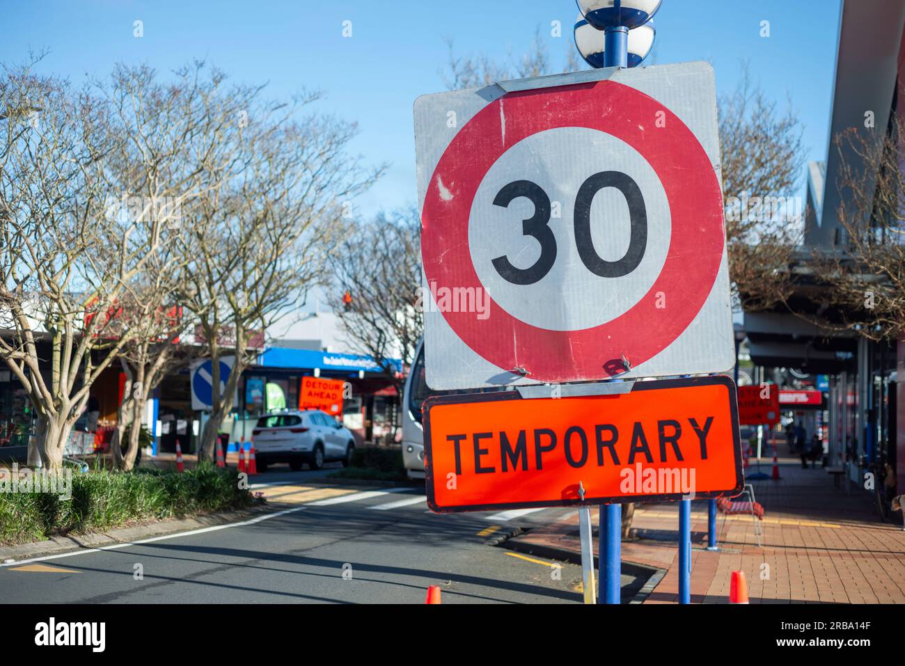 Segnale temporaneo del limite di velocità di 30 km su una strada trafficata di negozi in periferia. Fuori fuoco. Seguire le indicazioni per proseguire lungo la strada. Lavori stradali su Auckland Roads. Foto Stock