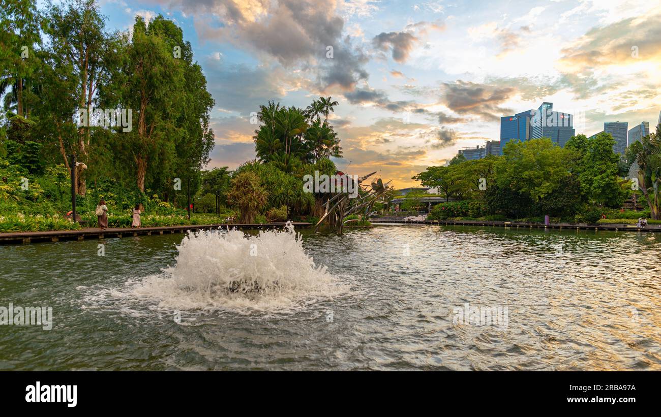 Vista finale della giornata dei getti d'acqua in un lago presso il parco Gardens by the Bay, Singapore. Preso in una giornata parzialmente oscurata con due donne irriconoscibili se Foto Stock