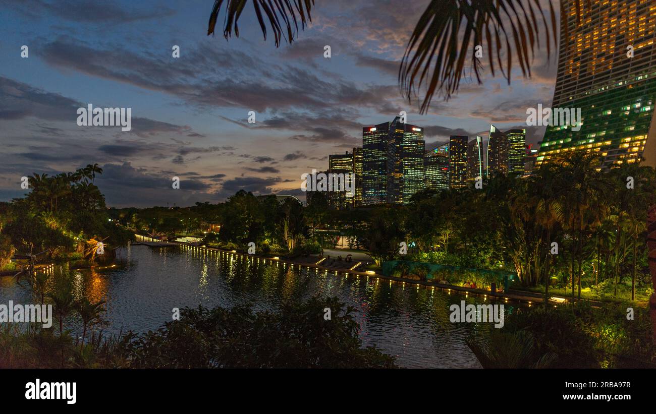 Una vista panoramica del complesso Marina Bay Sands incorniciata da vegetazione. Foto scattata dai vicini giardini del parco della baia al crepuscolo senza persone. Foto Stock
