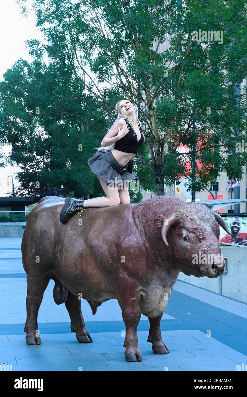 Giovane donna in posa su una scultura di toro in ottone di Joe Fafard, Georgia Street, Vancouver, British Columbia, Canada Foto Stock