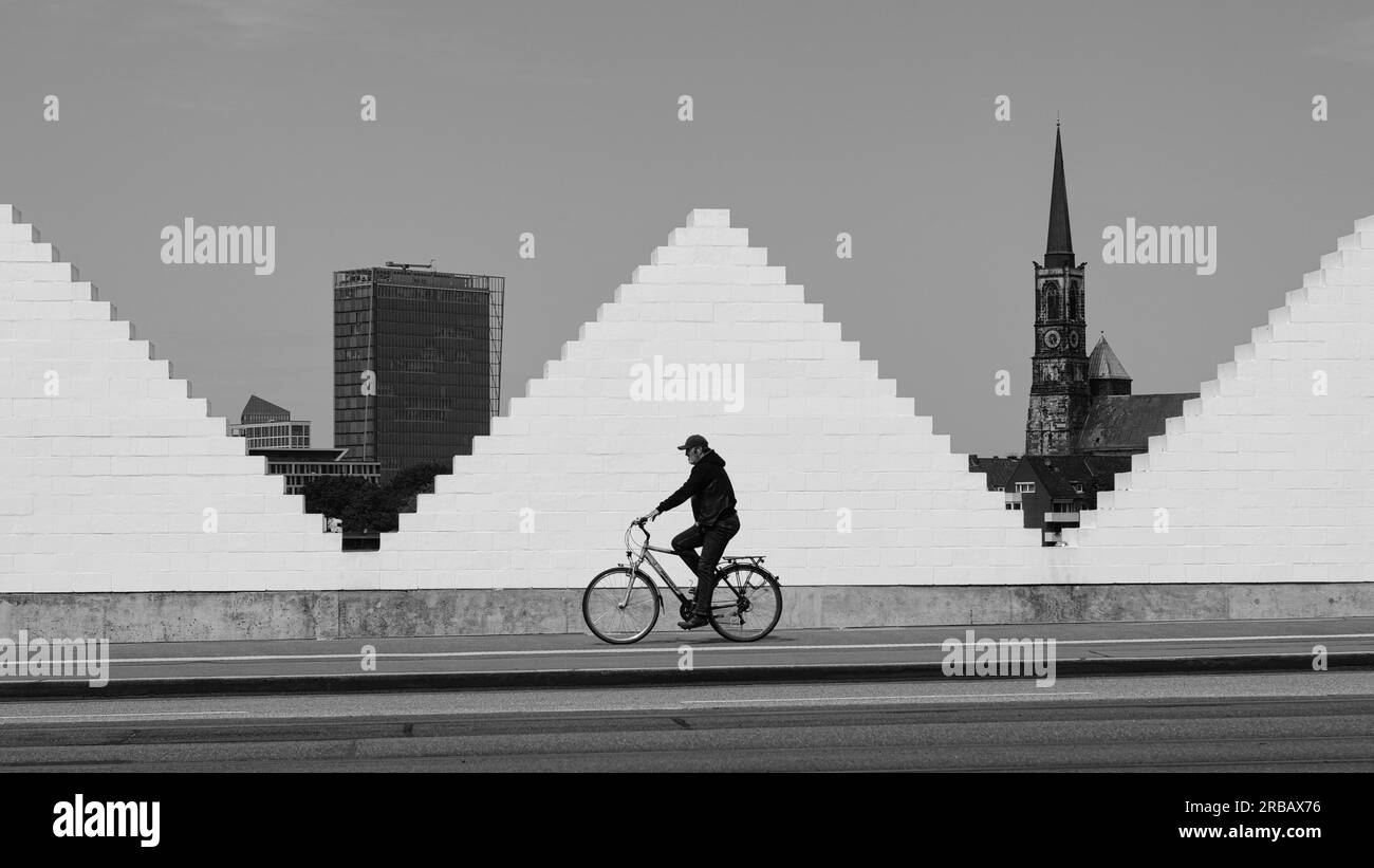 Ciclista di fronte al muro bianco, la chiesa e l'alto edificio dietro, città anseatica, Brema, Germania Foto Stock