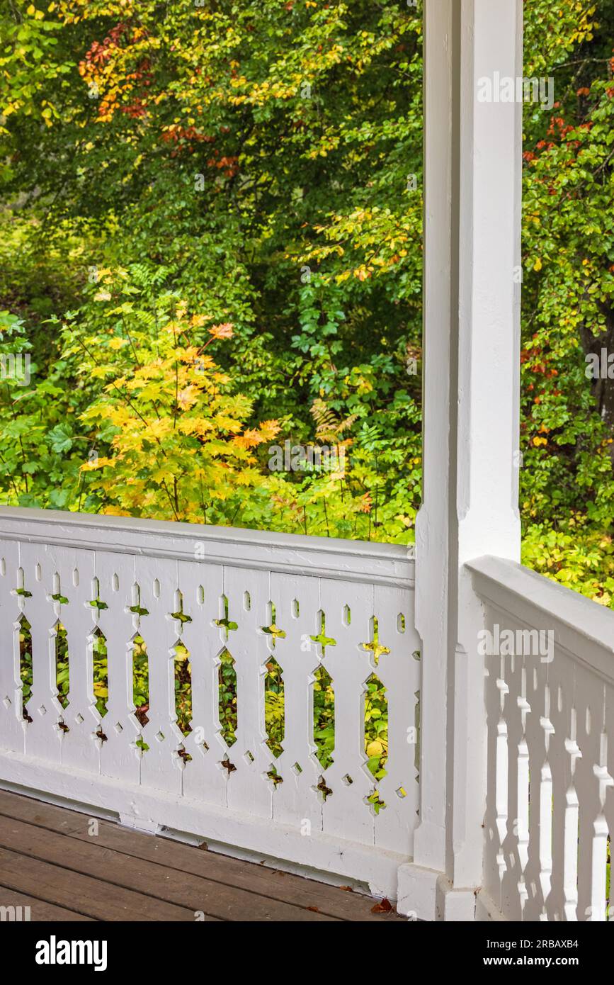 Ringhiera su un portico con falegnameria in legno bianco da alberi decidui nei colori autunnali Foto Stock