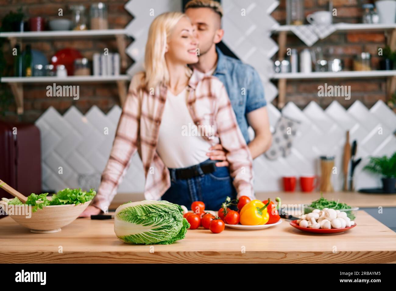 Cibo vegetariano. Cibo vegano ingredienti di cottura sul tavolo e felice abbracciando la coppia sullo sfondo Foto Stock