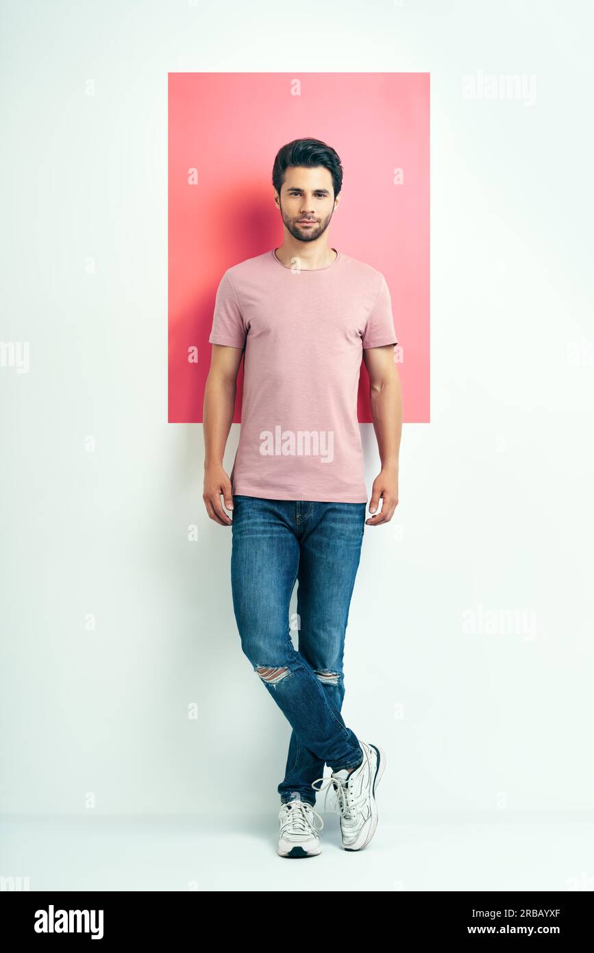 Ritratto a lunghezza intera di un giovane bell'uomo con t-shirt rosa su sfondo geometrico Foto Stock